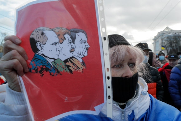 지난 12일(현지시간) 우크라이나 키예프에서 열린 러시아 침공 반대 행진에서 한 여성이 블라디미르 푸틴(왼쪽) 러시아 대통령과 소련의 독재자였던 이오시프 스탈린(가운데), 나치 독일의 독재자 아돌프 히틀러(오른쪽)가 나란히 그려진 그림을 들고 있다. 키예프 EPA 연합뉴스