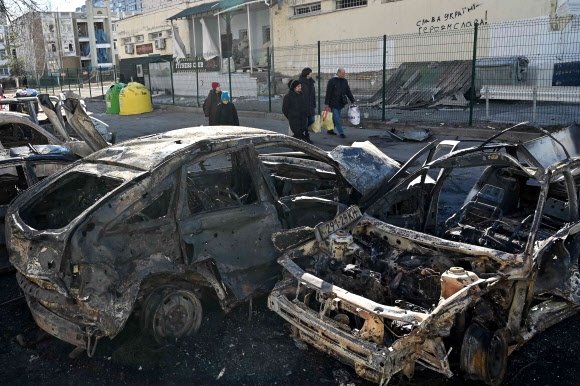 28일(현지시간) 우크라이나 수도 키예프 외곽에서 시민들이 불탄 차량 옆을 지나가고 있다. 2022.3.1 AFP 연합뉴스