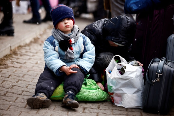 3일(현지시간) 폴란드 국경도시 코르쵸바에 마련된 임시 수용소 밖에서 피란 온 우크라이나의 한 어린이가 오도카니 앉아 있다. 2022.3.3 코르쵸바 로이터 연합뉴스