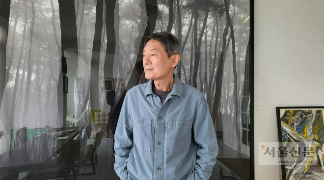 황학주 시인이 지난 18일 제주 중산간 마을 조천읍 신촌리 자택에서 배병우 작가의 소나무 사진 앞에서 창 너머 바다를 바라다보고 있다. 