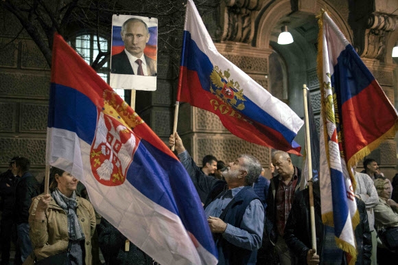 24일(현지시간) 세르비아 베오그라드에서 열린 러시아의 우크라이나 침공 지지 시위에 참석한 사람들이 세르비아 국기(왼쪽)과 러시아 국기(오른쪽), 그리고 블라디미르 푸틴 러시아 대통령의 초상화를 흔들고 있다. 베오그라드 AFP 연합뉴스