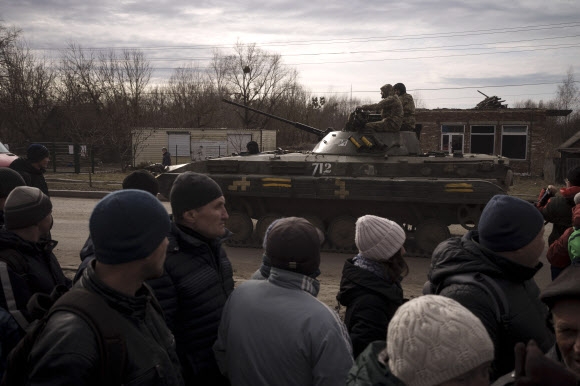 28일(현지시간) 우크라이나 수도 키이우 동쪽 트로스얀네츠 마을에서 구호품을 받으려 줄 서 있는 주민들이 탱크 타고 이동하는 자국 군인을 바라보고 있다. 우크라이나군은 이틀 전에 인구 2만명의 트로스얀네츠를 탈환했다고 밝혔다. 2022.3.29 트로스얀네츠 AP 연합뉴스