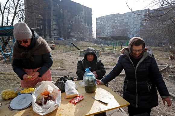우크라이나 동부 마리우폴에 남아 있는 할머니들이 러시아 군의 포위 공격으로 처참한 몰골을 드러낸 아파트 앞 공터에서 끼니를 준비하고 있다. 마리우폴 로이터 연합뉴스 