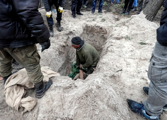 우크라이나 수도 키이우 외곽 모티진 마을 주민들이 4일(현지시간) 러시아 병사들에 살해된 민간인 여성 야로슬라바(43)의 시신을 무덤 구덩이에서 끌어올리려 하고 있다. 모티진 로이터 연합뉴스 