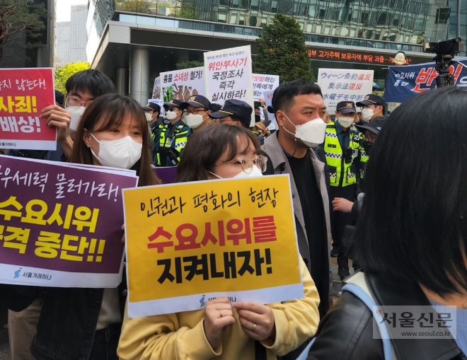 수요시위 참가자들이 20일 오전 기자회견을 열고 ‘수요시위를 지켜내자’ 등이 쓰인 손팻말을 들고 있는 뒷편으로 ‘위안부’ 피해를 부정하는 보수단체의 맞불집회가 열리고 있다. 곽소영 기자