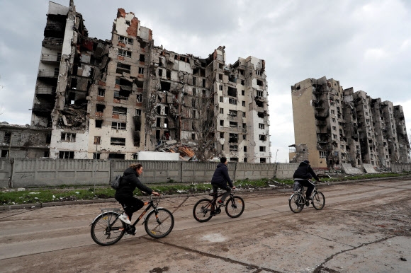 Cyclists pass by an apartment building in the southeastern port city of Mariupol, which was damaged by shelling following the Russian invasion of Ukraine.  2022.4.22 TAS Yonhap News