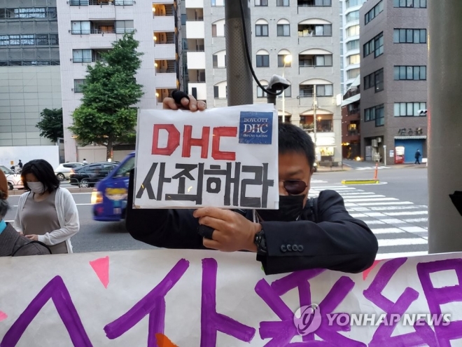 일본의 시민단체인 ‘DHC에 차별을 그만두게 하는 캠페인’은 혐한을 조장해온 요시다 요시아키(吉田嘉明) DHC 회장에 항의하는 집회를 3일 저녁 도쿄 미나토(港)구 소재 DHC 본사 앞에서 개최했다. 한 집회 참가자가 한국어로 ‘DHC는 사죄해라’라고 쓴 팻말을 들고 있는 모습.