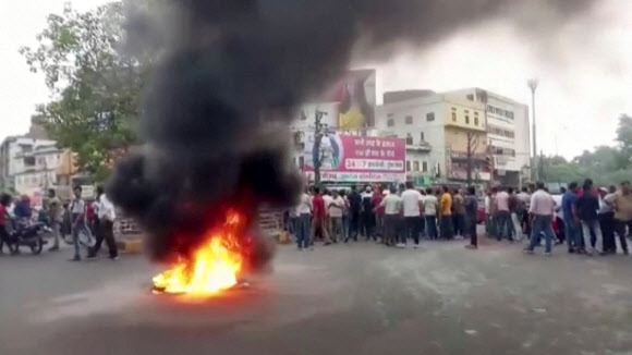 인도 서부 라자스탄주 우다이푸르에서 힌두교도 남성이 살해된 후 긴장감이 고조되면서 주민들이 거리에 모이는 동안 도로 위 화염에 휩싸인 물체에서 연기가 피어오르고 있다. 2022.6.28 ANI·로이터 연합뉴스