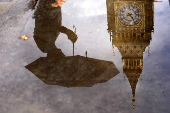 영국의 오랜 가뭄을 끝내는 비가 내린 16일(현지시간) 런던을 상징하는 빅벤과 그 앞을 지나가는 시민이 물웅덩이에 비치고 있다. 2022.8.16 AP 연합뉴스