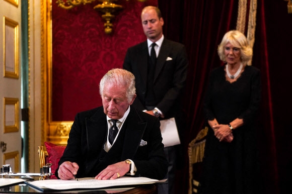 지난 10일(현지시간) 영국의 새 국왕으로 선포된 찰스 3세가 이날 런던 세인트제임스궁에서 열린 즉위식에서 국왕에 대한 충성 등을 맹세한 선언문에 서명하고 있다. 찰스 3세 뒤에서 윌리엄 왕세자와 커밀라 파커 볼스 왕비가 서명을 지켜보고 있다. 런던 AFP 연합뉴스