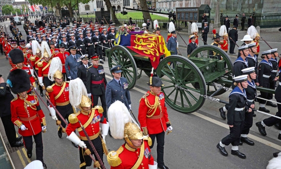 붉은 제복의 영국 근위대가 19일(현지시간) 런던 웨스트민스터홀 바깥에서 엘리자베스 2세 여왕의 관을 해군 부대 포차에 올려 운구하고 있다. 운구 행렬에는 해군 병사 142명이 함께했다. 런던 AFP 연합뉴스