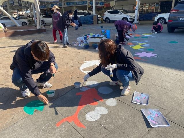 경북 군위군은 군위전통시장 방문객들에게 볼거리와 추억을 제공하기 위해 최근 시장 바닥에 포토존을 조성했다. 사진은 자원봉사자들이 포토존을 설치하는 모습. 군위군 제공