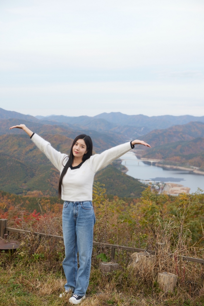 한국 농촌의 매력을 전하는 ‘트래블 다이어리: 군위&담양’ 편에 출연하는 가수 권은비가 경북 군위군 하늘채 치유 농장에서 군위댐(군위호)를 배경으로 포즈를 취하고 있다. 농림축산식품부 제공