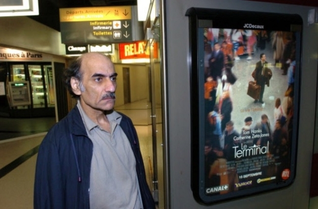 영화 ‘터미널’ 속 주인공의 모델이 된 이란 출신 망명객 메르한 카리미 나세리(1945∼2022)가 2004년 프랑스 파리 샤를드골 공항 안에 서 있는 모습. 오른쪽에 그해 개봉한 ‘터미널’의 포스터가 보인다. 파리 AFP연합뉴스 