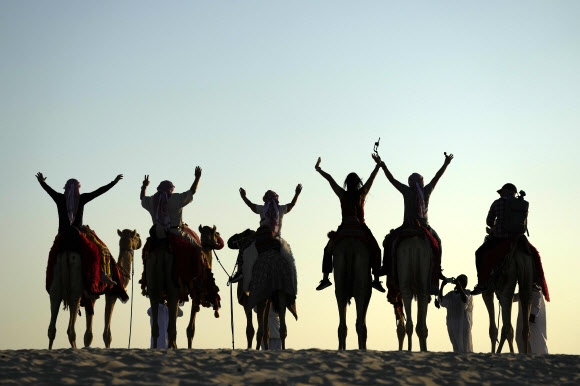 사람들이 26일 카타르 메사이에에서 낙타 위에서 사진을 찍기 위해 포즈를 취하고 있다. 2022.11.30 AP연합뉴스