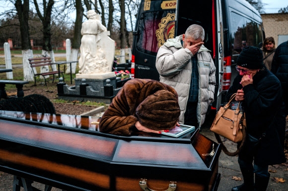 우크라이나가 최근 수복한 남부 도시 헤르손에서 지난 23일(현지시간) 러시아의 포격으로 사망한 딸의 장례식에서 부모가 딸의 시신이 든 관 앞에서 울고 있다. 2022.12.27 AFP 연합뉴스