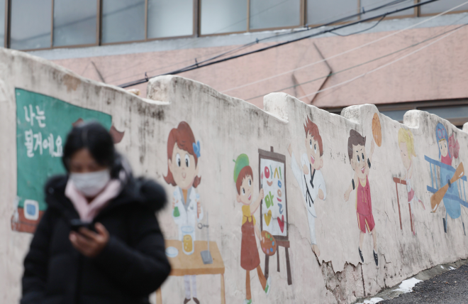 성동구의 한 마을 벽화 속 웃는 얼굴들 앞으로 마스크를 쓴 시민이 걸어가고 있다.   연합뉴스