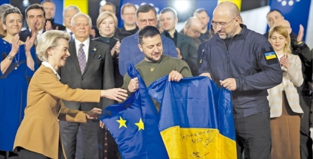 우르줄라 폰데어라이엔 유럽연합(EU) 집행위원장(왼쪽)이 우크라이나 수도 키이우에서 볼로디미르 젤렌스키 우크라이나 대통령(가운데), 데니스 슈미할 우크라이나 총리(오른쪽)와 함께 양측 국기를 들고 있다.  우크라이나는 지난해 2월 28일 EU 가입 후보국 지위를 받았다. EPA연합뉴스