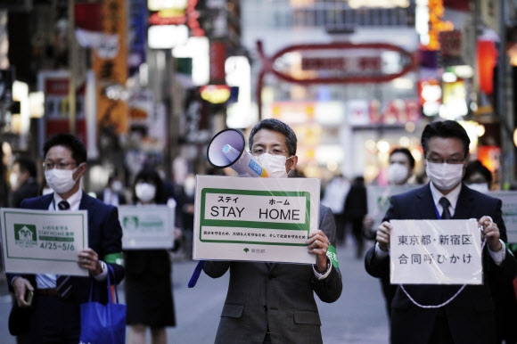 코로나19 확산으로 일본 전역에 긴급사태가 선포된 가운데 24일 도쿄의 대표적 유흥가인 신주쿠구 가부키초 거리에서 마스크를 쓴 도쿄도 직원들이 시민들에게 외출 자제를 당부하고 있다.  도쿄 AP 연합뉴스