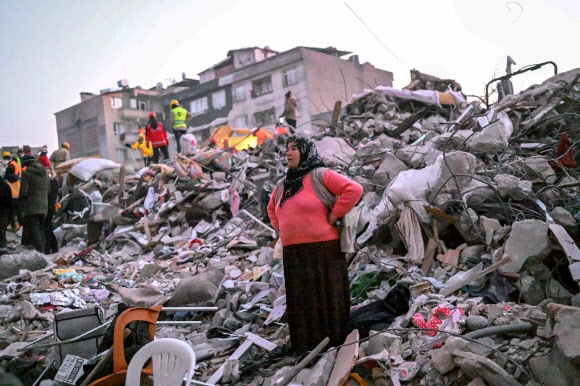 튀르키예·시리아 강진으로 사망자 수가 3만 7000명을 넘어선 가운데 튀르키예 남부 하타이주(州)의 무너진 건물 잔해 위에 한 여성이 친척들이 발견되길 바라며 서 있다. 2023.2.13 AFP 연합뉴스