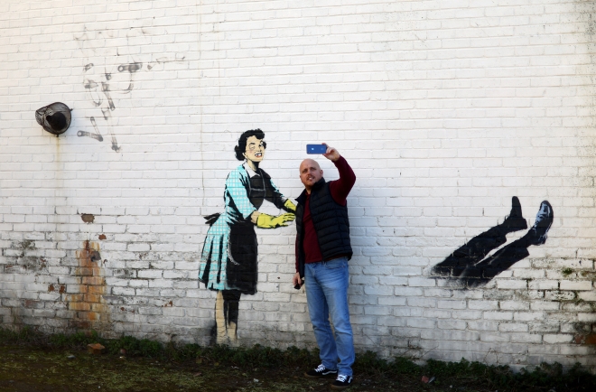 영국 켄트주 마게이트 건물 벽에 그려진 ‘밸런타인데이 마스카라’라는 제목의 뱅크시 작품 앞에서 한 남성이 14일(현지시간) 기념사진을 찍고 있다. 마게이트 로이터 연합뉴스