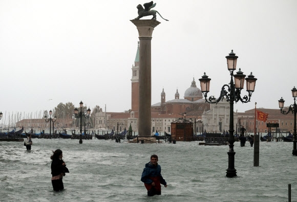 폭우로 조수가 해수면 위 156㎝까지 급상승하면서 물바다로 변한 이탈리아 베네치아의 산마르코 광장을 29일(현지시간) 사람들이 걸어 다니고 있다. 로이터 연합뉴스