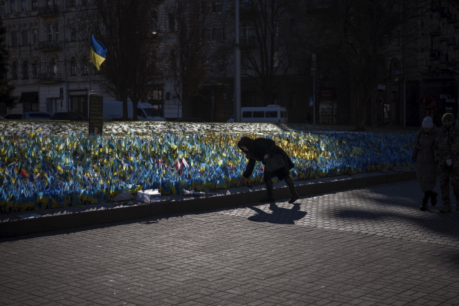 A woman places a Ukrainian flag at a memorial for those killed during the war, near Maidan Square in central Kyiv, Ukraine, Sunday, Feb. 12, 2023. (AP )