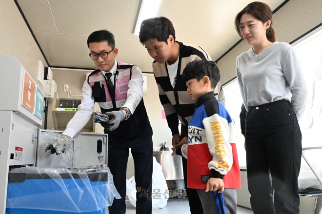 환경보안관이 27일 서울 마포구 구청 광장에 쓰레기를 감량하기 위해 설치한 재활용품 중간 처리장 ‘소각 제로가게’ 1호점에서 시민들에게 캔, 투명페트병 처리기 이용 방법을 설명하고 있다. 홍윤기 기자