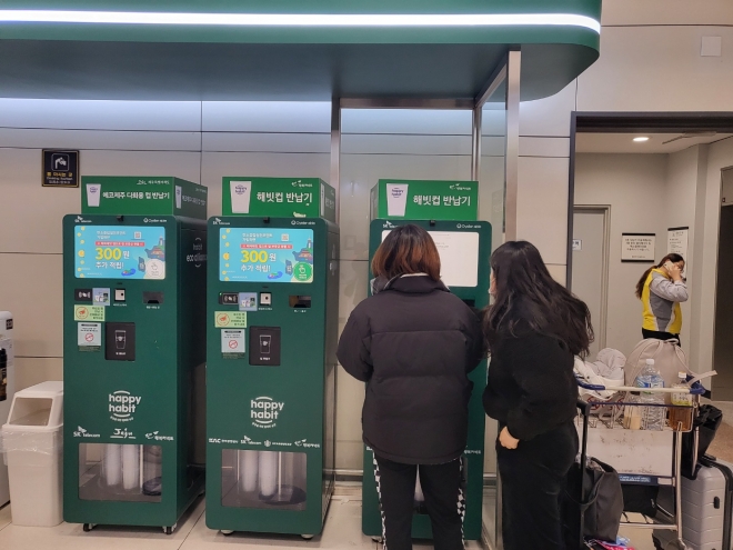 제주공항에서 설치된 다회용컵 반납기에서 여행객들이 스타벅스 등에서 썼던 다회용컵을 반납하고 있다. 다회용컵을 반납하면 1000원을 현금으로 돌려준다.