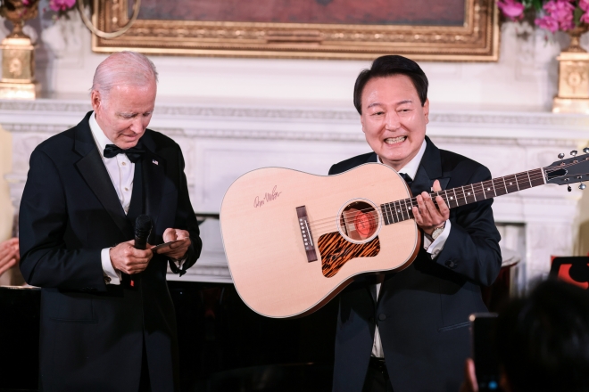2023년 4월 26일 미국 워싱턴 백악관 이스트룸에서 열린 국빈만찬에서 조 바이든 미국 대통령이 지켜보는 가운데 한국의 윤석열(R) 대통령이 돈 맥클린이 사인한 어쿠스틱 기타를 들고 있다. EPA/올리버 콘트레라스/풀