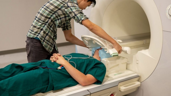 연구진이 기능성 자기공명영상(fMRI) 장치로 실험 대상자의 뇌 활동을 측정하기 위한 실험 준비를 하는 모습. 연구진은 fMRI 장치로 수십 시간 분량의 뇌 활동 데이터를 확보해 뇌를 읽는 인공지능 ‘시맨틱 디코더’를 훈련했다. 미국 텍사스 오스틴대 제공
