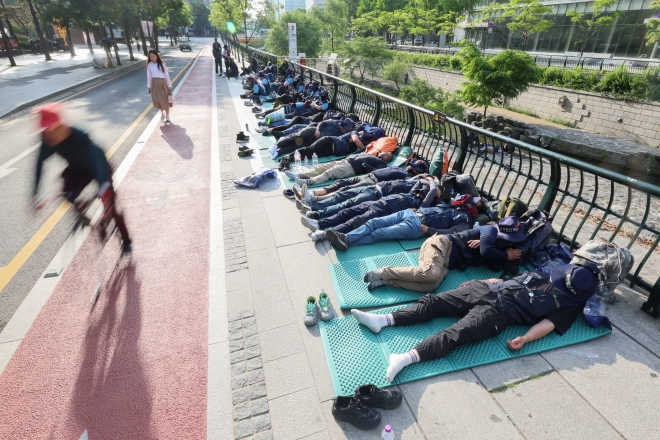 지난 17일 오전 출근시간대 시민들이 서울 중구 청계광장에서 전날 밤 총파업 결의대회 후 노숙하고 있는 민주노총 건설노조원들을 지나치고 있다. 연합뉴스