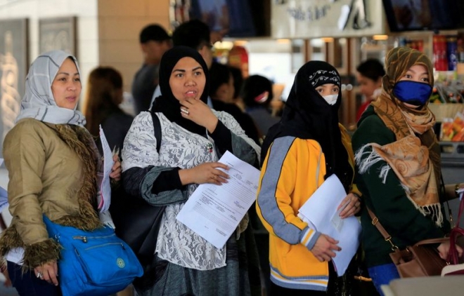 2018년 2월 18일 쿠웨이트 가정부 취업을 위해 출국하려는 필리핀 여성들이 마닐라 국제공항에서 출국 서류를 손에 든 채 줄지어 서 있다. 코로나19 팬데믹이 시작되기 한참 전인데도 여성들이 마스크를 착용하고 있는 점이 눈길을 끈다. 로이터 자료사진
