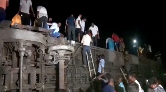 인도 북동부 오디샤주 발라소레 지역에서 2일(현지시간) 열차 충돌 참사가 빚어진 뒤 사람들이 전도된 객차에서 부상자를 찾고 있다. 발라소레 ANI 로이터 연합뉴스