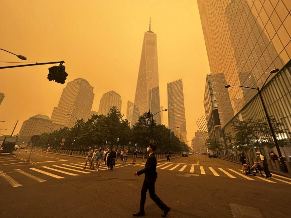 7일(현지시간) 캐나다 산불의 영향으로 미국 뉴욕의 하늘이 오렌지색으로 변한 가운데 뉴욕시민들이 원월드트레이드센터 앞으로 지나고 있다. 2023.6.7 AP 연합뉴스