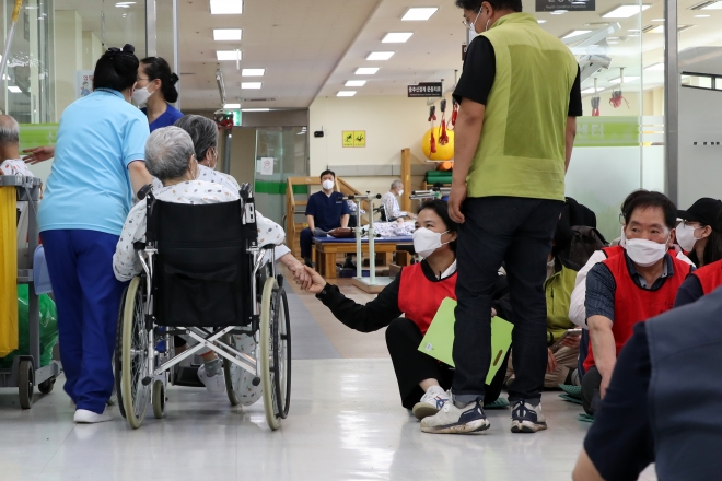 5일 광주 제1시립요양병원·정신병원 복도에서 휠체어에 앉아 재활치료실로 이동하는 환자가 파업에 나선 노조원의 손을 잡아주고 있다.  연합뉴스