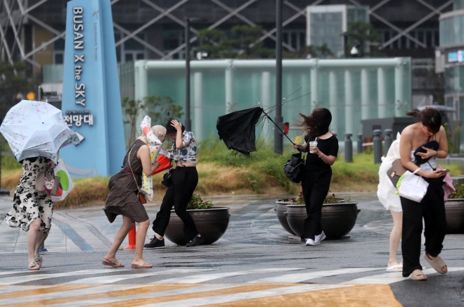 제6호 태풍 ‘카눈’이 북상 중인 9일 부산 해운대구 엘시티 인근에서 강한 빌딩풍이 몰아치자 관광객들이 우산을 부여잡고 힘겹게 걷고 있다. 부산 뉴스1