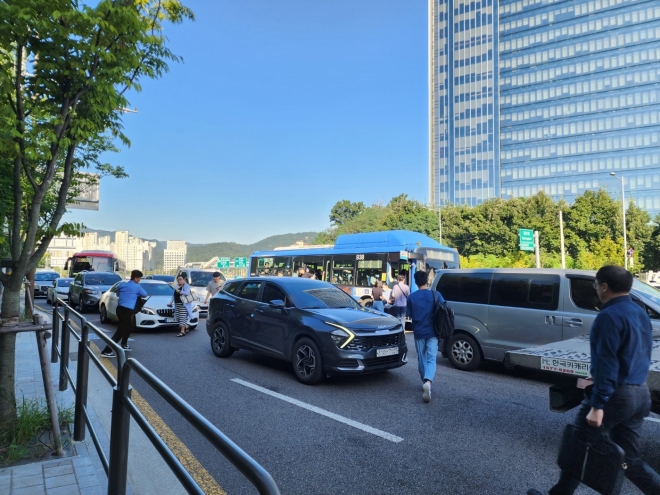 7일 오전 서울 서초구 양재동 한 버스정류장에서 도로 가운데 멈춘 버스에 승하차하기 위해 시민들이 도로를 횡단하고 있다.