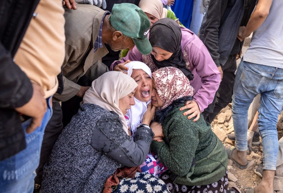 모로코 중부 아미즈미즈 근처 이미 은탈라 마을에 거주하는 여성들이 10일(현지시간) 자원봉사자들이 맨손으로 흙을 파내 가족 시신을 찾아내자 신원을 확인한 뒤 오열하고 있다. 이미 은탈라 마을 AFP 연합뉴스