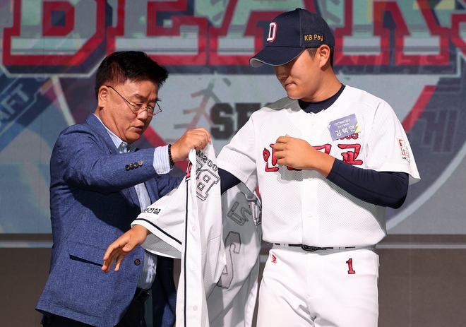 김태룡 두산 베어스 단장이 14일 서울 웨스틴조선호텔에서 열린 2024 KBO 신인 드래프트에서 전체 2순위로 김택연(인천고)을 지명한 뒤 유니폼을 입혀주고 있다. 뉴스1