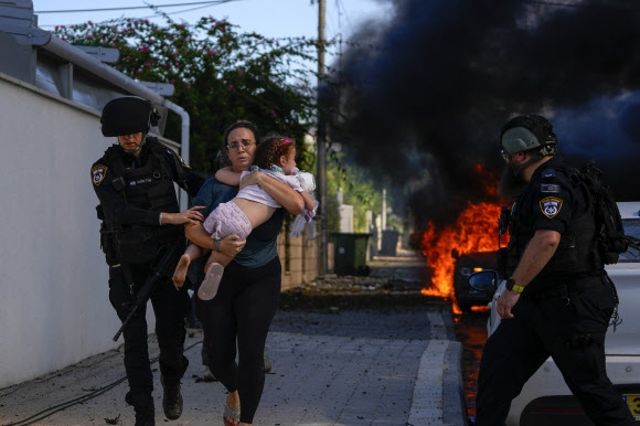 이스라엘 남부 아슈켈론의 경찰관들이 지난 7일(현지시간) 팔레스타인 무장 정파 하마스의 기습 공격의 일환으로 로켓이 발사하자 아이를 안은 여인을 피신시키고 있다. AP 자료사진 연합뉴스