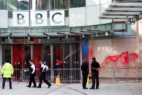 영국 런던 경찰관들이 14일(현지시간) 팔레스타인 지지 시위대가 출발한 뒤 BBC 본사 건물 현관에 붉은색 페인트가 칠해진 현장을 둘러보는 가운데 한 인부가 유리 출입문의 페인트를 씻겨내고 있다. 런던 로이터 연합뉴스