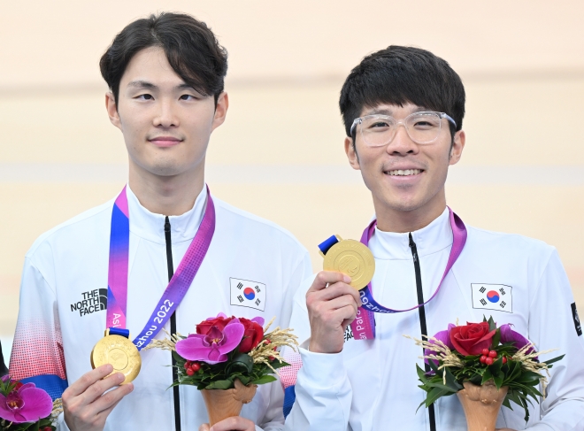 한국 남자 사이클 국가대표 김정빈(왼쪽)이 23일 중국 항저우 CSC 벨로드롬에서 열린 2022 항저우아시안패러게임 시각장애(MB) 4000m 개인 추발에서 우승을 차지하고 경기파트너 윤중헌과 함께 금매달을 들어 보이고 있다. 대한장애인체육회 제공