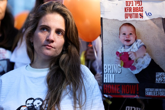생후 10개월 밖에 안된 아기 크피르 비바스의 조속한 석방을 요구하는 집회가 28일(현지시간) 이스라엘 텔아비브에서 열린 가운데 한 참가자가 크피르 포스터 옆에 서 침통한 표정을 짓고 있다. 텔아비브 로이터 연합뉴스