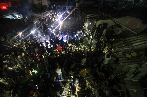 14일(현지시간) 팔레스타인 가자지구 남부 라파 주민들이 이스라엘군의 공습에 무너진 건물 잔해 더미에서 생존자들을 찾고 있다. 라파 AFP 연합뉴스