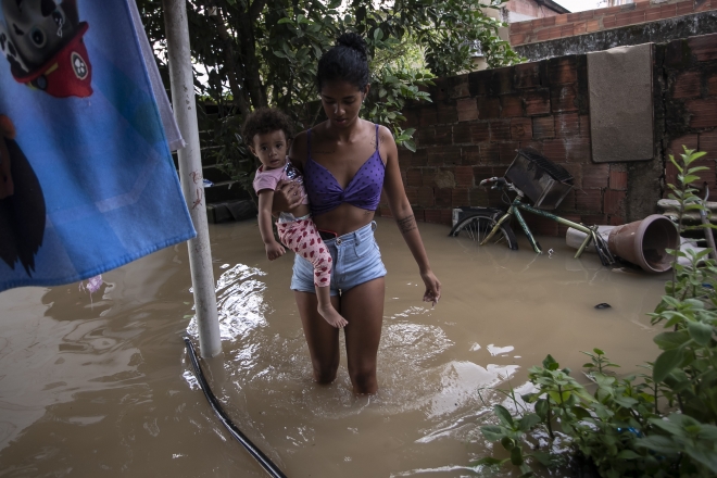14일(현지시간) 브라질 리우데자네이루에 내린 폭우로 한 여성이 아이를 안고 깊이 찬 물을 헤치고 걸어 나오고 있다. 리우데자네이루 AP 연합뉴스