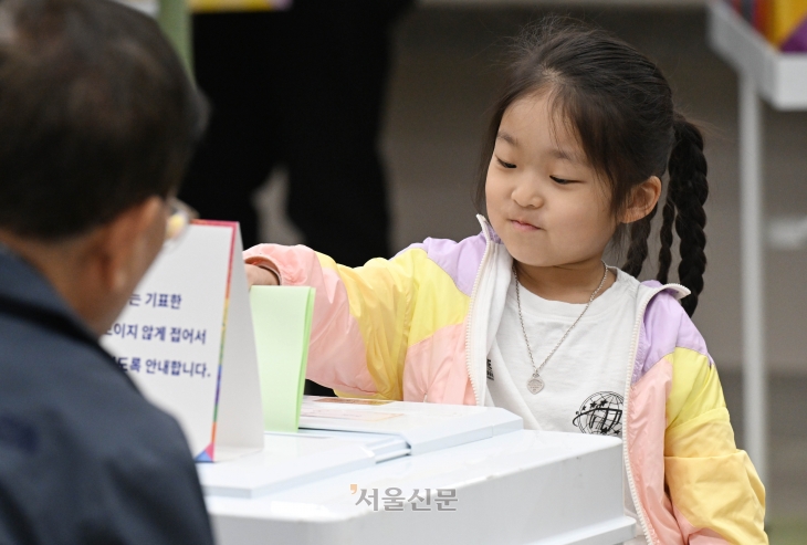 제22대 국회의원 선거일인 10일 서울 영등포구 여의도중학교에 마련된 투표소에서 한 어린이가 부모의 투표용지를 투표함에 대신 넣고 있다.    홍윤기 기자