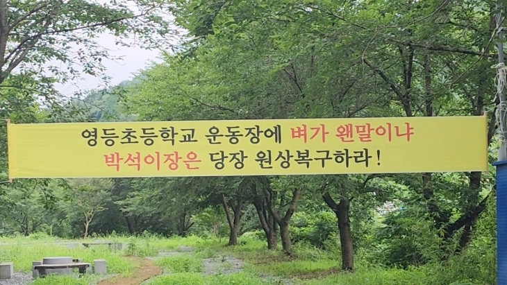 학교 운동장이 거대한 논으로 둔갑 된 모습에 항의하는 현수막이 걸려있다.