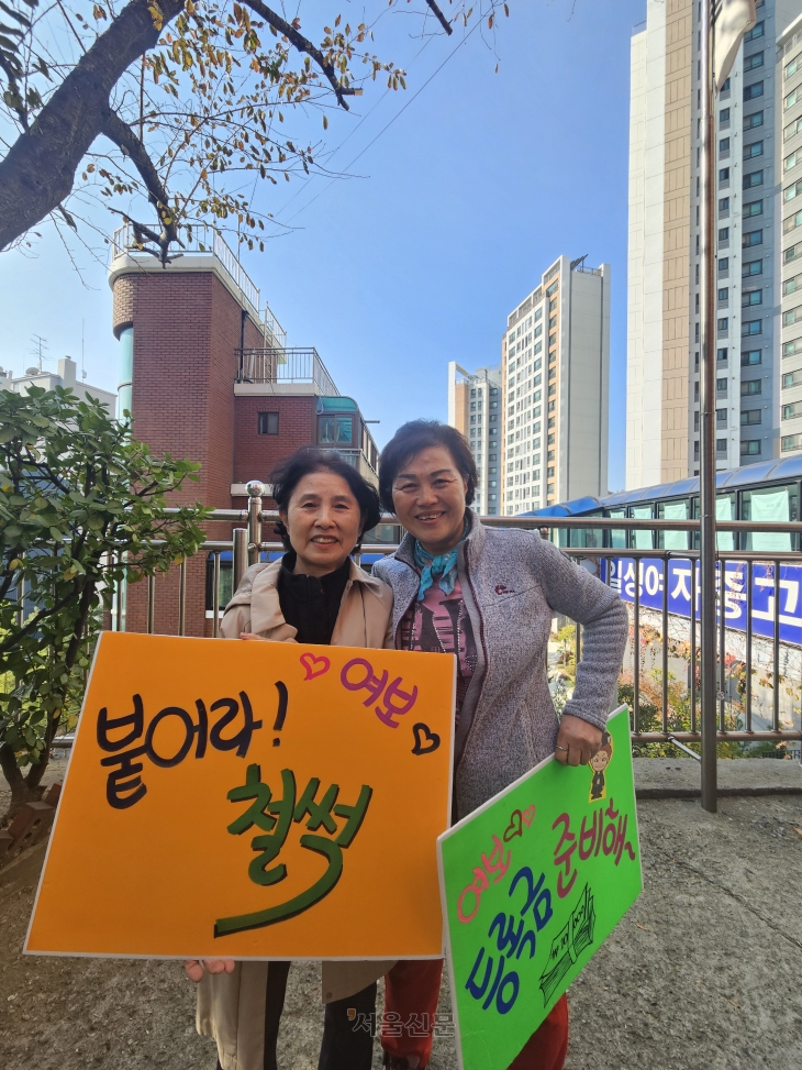 12일 서울 마포구 일성여자중고등학교에서 열린 ‘수능응원 떡 전달식’에서 2학년 학생 최복희(왼쪽)씨와 김을순씨가 응원 팻말을 들고 있다. 이날 출정식에 참여한 3학년 학생 107명의 뒤를 이어, 이들은 2026학년도 수능을 응시할 예정이다.