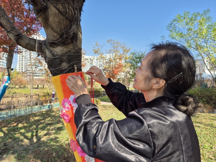 3년째 ‘트리니팅’을 하는 서울 위례동주민센터 뜨개봉사단의 최고령 참가자 박영옥(86)씨가 지난 12일 서울 송파구 위례호수공원 일대 나무에 60년 전 뜨개 공방을 하던 실력을 되살려 뜨개실을 엮고 있다.